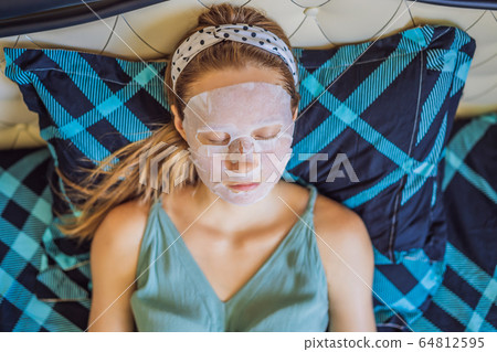 Young red-haired woman doing facial mask sheet. Beauty and Skin Care Concept Young red-haired woman doing facial mask sheet. Beauty and Skin Care Concept 64812595
