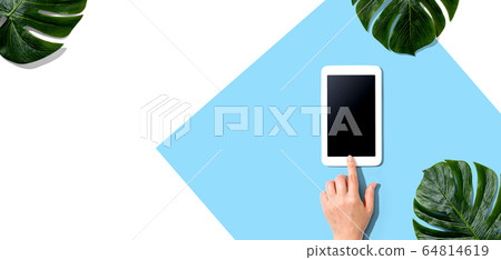 Person using a tablet computer with tropical leaves Person using a tablet computer with tropical leaves 64814619