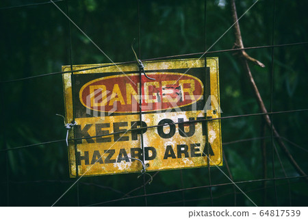Danger sign with text KEEP OUT HAZARD AREA as warning message hanging on fenced dark zone, dirty poster outside Danger sign with text KEEP OUT HAZARD AREA as warning message hanging on fenced dark zone, dirty poster outside 64817539