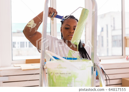 Pretty smiling african american woman painting interior wall of home with paint roller. Redecoration, renovation, apartment repair and refreshment concept. 64817555