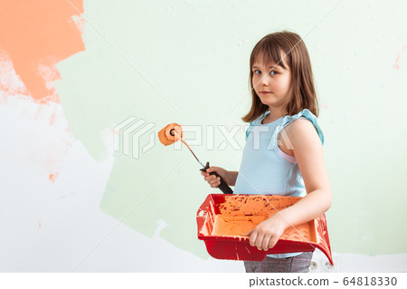 Repair in the apartment. Happy child girl paints the wall with orange paint. Renovation and redecoration concept. 64818330