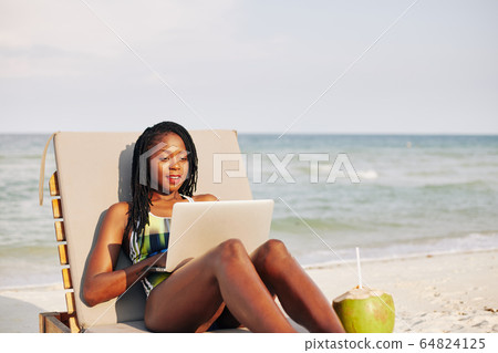 Woman resting on chaise-lounge with laptop 64824125