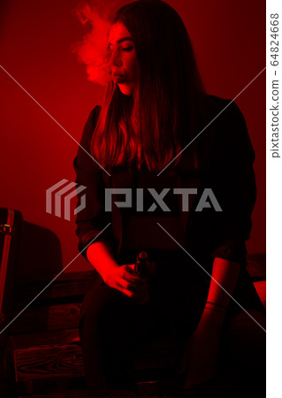 Girl model smokes vape in red light. 64824668