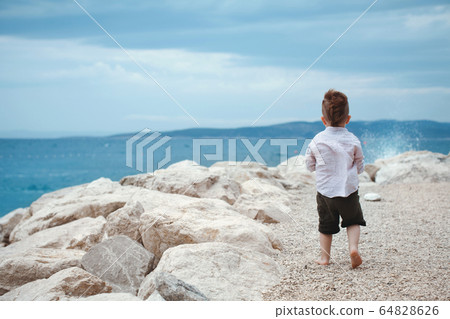 Baby boy stands with his back on the seashore Baby boy stands with his back on the seashore 64828626