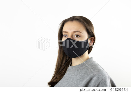 Portrait of young woman wearing black face mask isolated on gray background. Dust protection against virus. Coronavirus pandemic time. Female looking at camera Portrait of young woman wearing black face mask isolated on gray background. Dust protection against virus. Coronavirus pandemic time. Female looking at camera 64829484