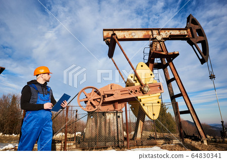 Oil man checking work of oil well pump jack. 64830341