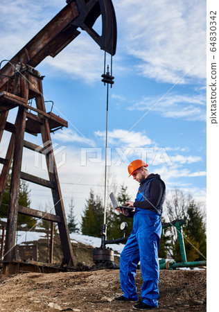 Petroleum engineer with laptop working in oil field. 64830342