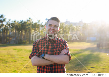 Handsome young smiling man standing on the grass at park. Summer in the city concept. 64830955