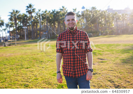 Handsome young smiling man standing on the grass at park. Summer in the city concept. 64830957