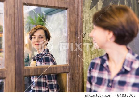 Young woman looking in a mirror. The mirror reflects her smiling face. Natural beauty and female concept. Young woman looking in a mirror. The mirror reflects her smiling face. Natural beauty and female concept. 64832303