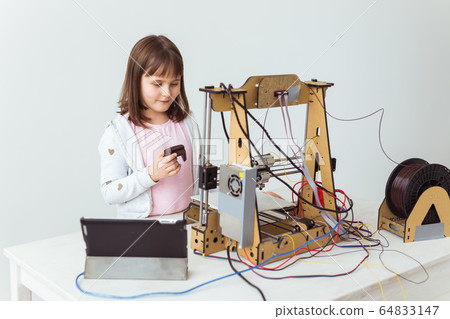Cute girl with 3d printed shutter shades is watching her 3d printer as it prints her 3d model. Cute girl with 3d printed shutter shades is watching her 3d printer as it prints her 3d model. 64833147