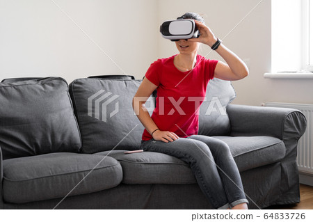 Woman sitting at home on the sofa with vr glasses. Online shopping, watching movie, video call 64833726