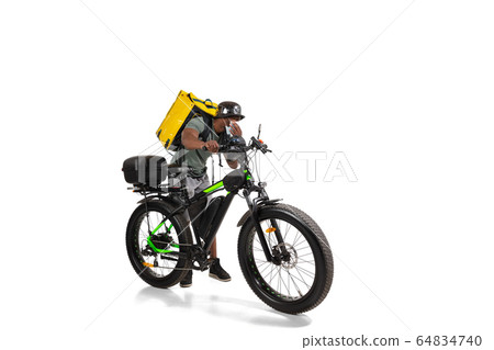 Too much orders. Contacless delivery service during quarantine. Man delivers food and shopping bags during isolation, wearing helmet and face mask. 64834740