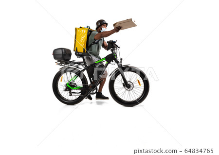 Too much orders. Contacless delivery service during quarantine. Man delivers food and shopping bags during isolation, wearing helmet and face mask. 64834765