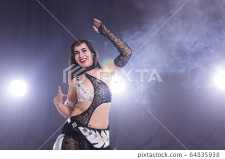 Young woman belly dancer in exotic dress with gold, dancing tribal fusion dance in studio. 64835938
