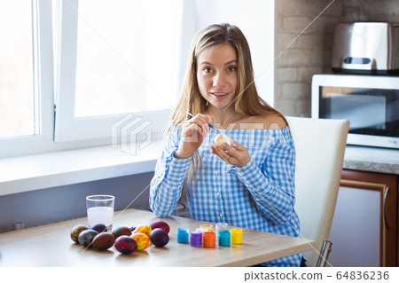 Holidays, handmade and creation concept - Happy young woman draws on Easter egg. 64836236