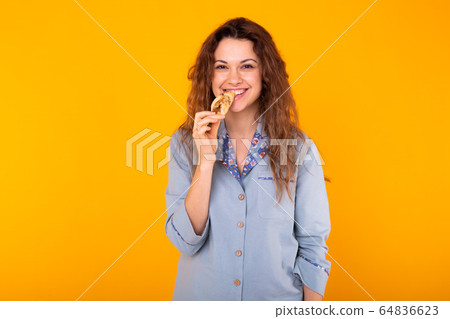 Joyful woman wears fashion pajama going to eat small delicious croissant on yellow background with copy space. Morning, breakfast and home wear concept. 64836623