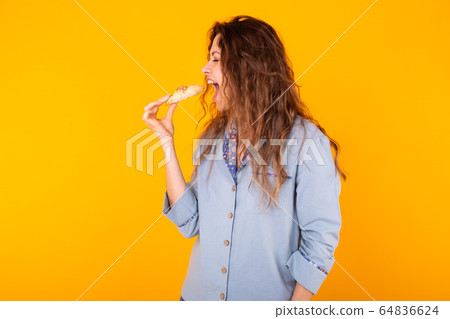 Joyful woman wears fashion pajama going to eat small delicious croissant on yellow background. Morning, breakfast and home wear concept. 64836624