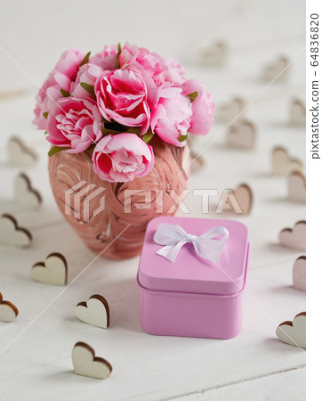 Beautiful composition with small square metallic pink gift box and delicate roses in pink vase on white wooden background Beautiful composition with small square metallic pink gift box and delicate roses in pink vase on white wooden background 64836820