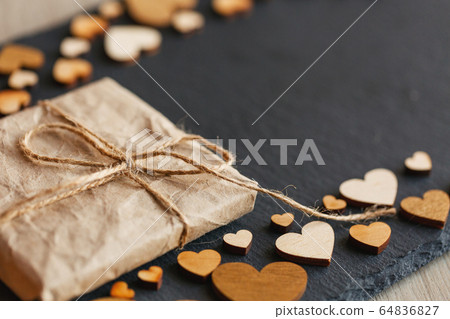 Small gift wrapped in kraft paper. Little wooden hearts on background. 64836827