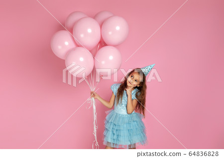 little child girl in dress and birthday hat celebrating with pastel pink air balloons 64836828
