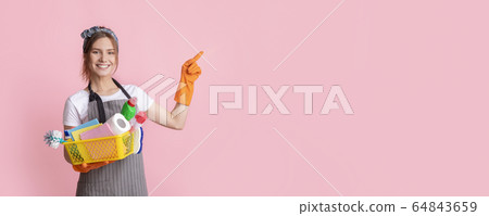 Smiling housewife holding basket with cleaning supplies and pointing at copy space 64843659