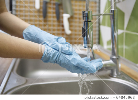 Woman in gloves washing hands before cooking in the kitchen 64843968