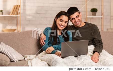 Couple using pc sitting on the sofa Couple using pc sitting on the sofa 64844040