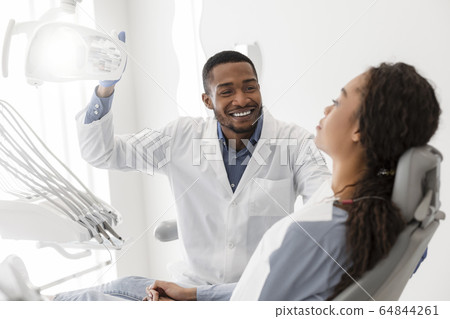 Cheerful black dentist turning on equipment before check up 64844261