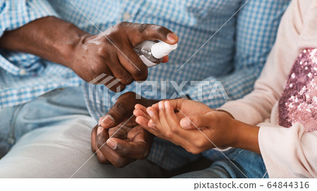 Closeup of African American granddad applying antiseptic on his grandkid's hands, panorama 64844316