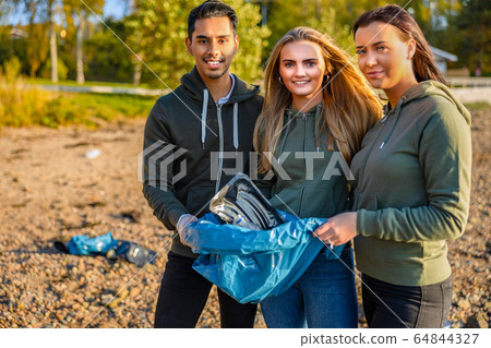 Smiling volunteers holding garbage bag at beach 64844327