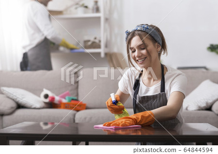 Millennial Couple Making Spring-Cleaning In Flat Together, Woman Wiping Table Millennial Couple Making Spring-Cleaning In Flat Together, Woman Wiping Table 64844594