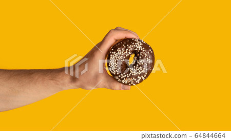 Close up of male hand showing sweet chocolate donut on orange background, copy space. Panorama Close up of male hand showing sweet chocolate donut on orange background, copy space. Panorama 64844664