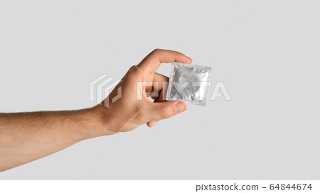 Safe sex concept. Young guy holding condom in wrapper on light grey background, empty space. Panorama Safe sex concept. Young guy holding condom in wrapper on light grey background, empty space. Panorama 64844674