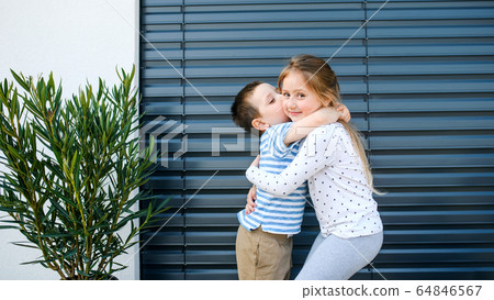 Small girl and boy standing outdoors at home, hugging. Small girl and boy standing outdoors at home, hugging. 64846567