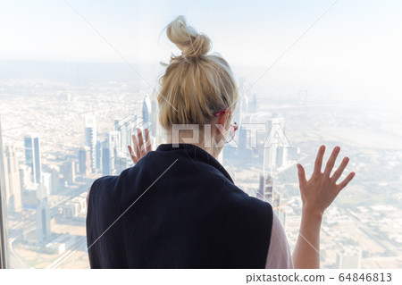 Beautiful girl admiring the city view from observing platform at the top of the tallest skyscraper in the world, Burj Khalifa in Dubai, UAE. 64846813