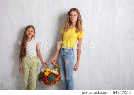 Two beautiful girls holding a basket of ripe vegetables 64847003