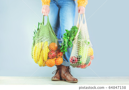Unrecognizable girl holds two mesh shoppers with 64847138