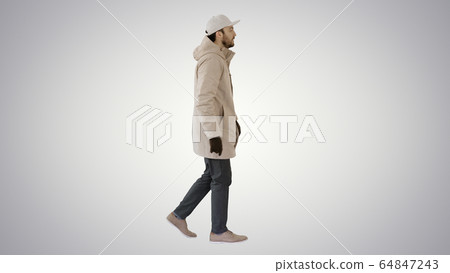 Handsome fashionable man in a winter stylish coat walking on gradient background. 64847243