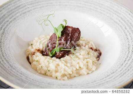 Beef risotto served in a plate with sauce and micro-greens decoration. Close-up. 64850282