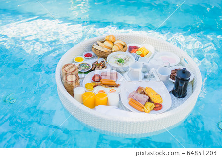 Floating breakfast set in tray with fried egg omelette sausage ham bread fruit milk juice coffee 64851203