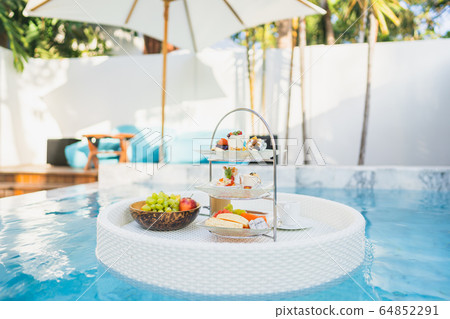 Breakfast and afternoon tea set floating around swimming pool Breakfast and afternoon tea set floating around swimming pool 64852291