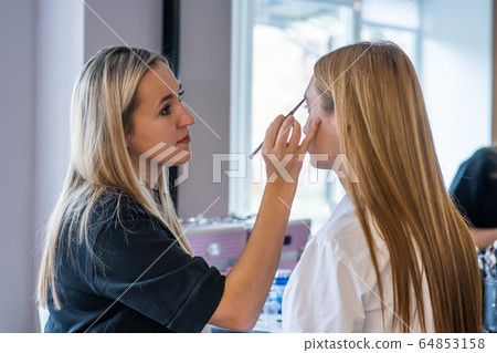 Makeup artist paints the eyes of a girl model 64853158