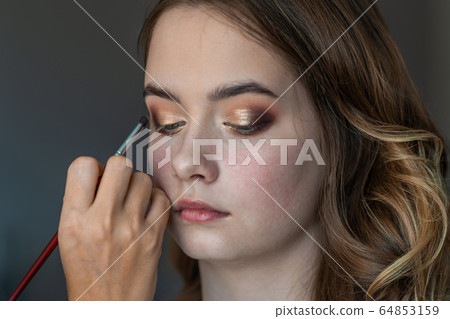 Makeup artist paints eyelids on a model girl. 64853159