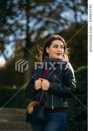 Stylish beautiful lady in a black leather jacket with a black bag and burgundy blouse. Attractive young woman smile Stylish beautiful lady in a black leather jacket with a black bag and burgundy blouse. Attractive young woman smile 64864540