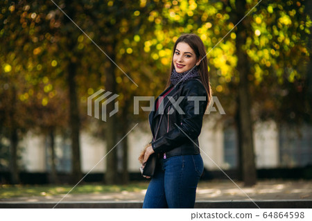 Stylish beautiful lady in a black leather jacket with a black bag. Attractive young woman smile Stylish beautiful lady in a black leather jacket with a black bag. Attractive young woman smile 64864598