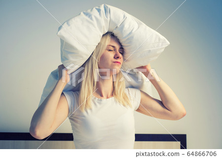 Young woman covering ears with pillow because of 64866706