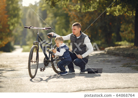 Father with son repare the bike in a park Father with son repare the bike in a park 64868764