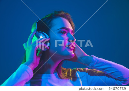 Caucasian woman's portrait isolated on blue studio background in pink-green neon light, stylish and beautiful 64870789