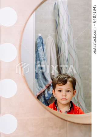 sad boy looks in the bathroom mirror 64871945